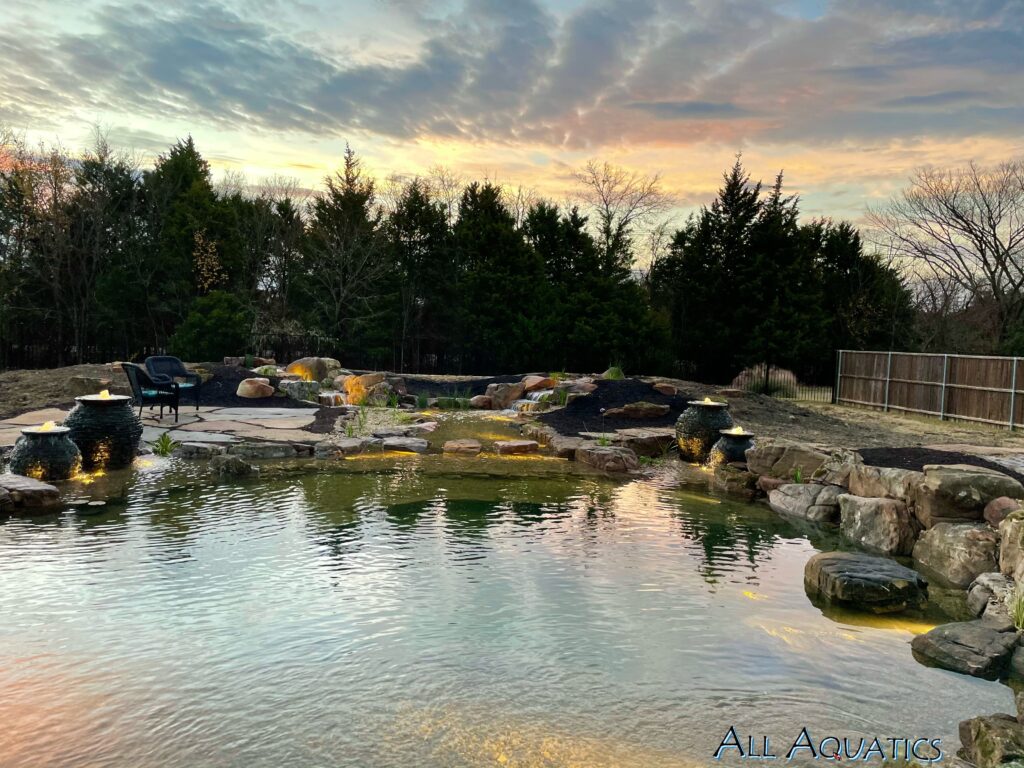 Backyard pond with rocks and evening lights.
